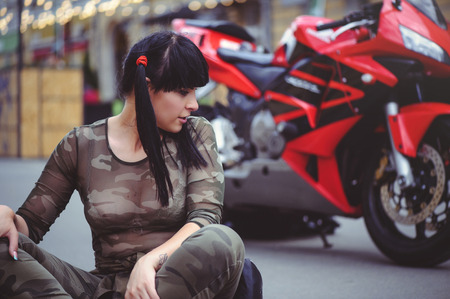 happy woman biker sitting near motorcycle and happy, close-up brunette with red bike.