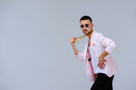 fashionable sophisticated man in a pink jacket and black trousers, wears a gold chain, the manifestation of emotions gestures hands space for text.の写真素材