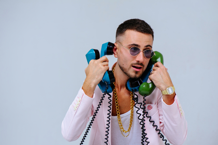 fashionable sophisticated man in a pink jacket and black trousers, with a lot of handsets, the expression of emotions gestures hands space for text.の写真素材