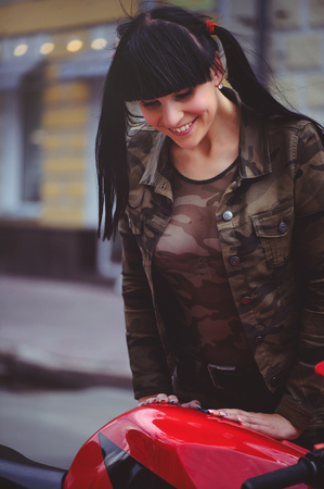 happy woman biker sitting near motorcycle and happy, close-up brunette with red bike.の写真素材