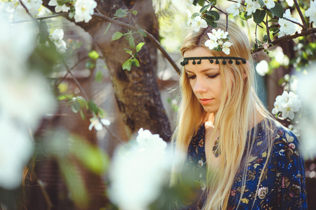 Portrait of young beautiful women smiling in the flowered garden in the spring time. Almond flowers are blooming. The girl is dressed stylishly, jewelry on her head. - imageの写真素材