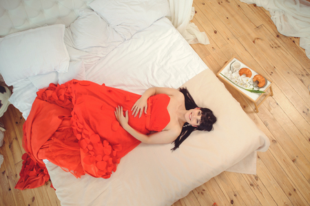 New concept of life. Pregnancy, motherhood and happiness. Closeup of pregnant woman in stylish elegant red dress on bed top view - Imageの写真素材