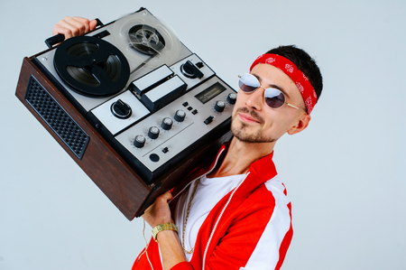 cheerful fashionable man wearing a red sports suit dancing jumps with a retro tape recorder. interesting and fervent style of the 90s.の写真素材