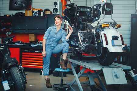beautiful girl repairs a motorcycle in a workshop, pin-up style, service and sale.の写真素材