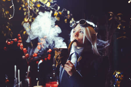 Halloween elf with magic magic in the dark forest. Beautiful young woman in a hat and elf costume holding magical chemistry. Halloween art designの写真素材