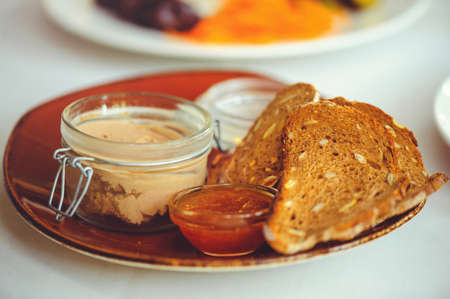 Fresh homemade chicken liver pate in a glass bowl or mold and slices of bread with seeds and sauce...