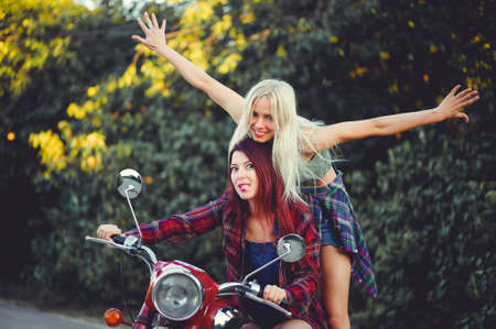 Young beautiful women ride a retro motorcycle. A talented girl in a blue overalls. They push the motorcycle, the merry go to the road. sale of spare parts. Place for text.の写真素材