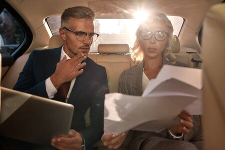 New business contract. Two business people in classic wear analyzing documents while sitting in the...