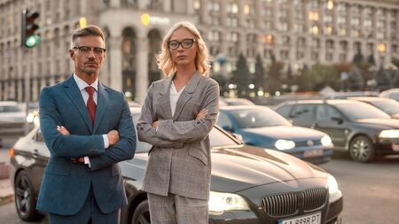 We are great team. Two confident colleagues in stylish classic wear keeping arms crossed and looking...