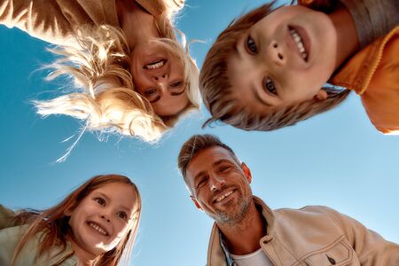 Playing together. Bottom view of happy and positive family smiling at camera while standing outdoorsの写真素材