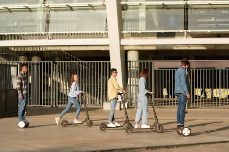 Feel the pleasure. Joyful friends riding kick scootersの写真素材