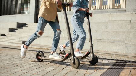 Cropped portrait of legs of couple riding electric scooters along the city street. Modern and...