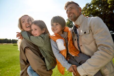 Happy moments. Young parents and their children enjoying time together and smiling while standing on a green meadowの写真素材