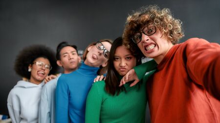 Funny selfie. Positive group of multicultural people in casual wear making grimaces and looking at...