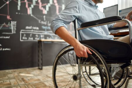 Cropped photo of male office worker in a wheelchair working in the modern office. Disabled man...