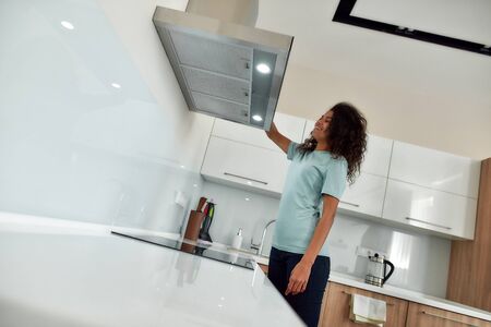 Portrait of young and happy afro american woman in uniform looking at kitchen range hood and smiling...