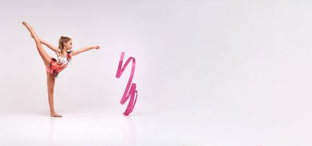 Begin here, go anywhere. Full-length shot of flexible cute little girl child gymnast doing acrobatic exercise using ribbon isolated on a white background. Sport, training, rhythmic gymnastics conceptの写真素材