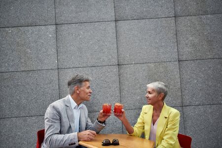 Its Time to Relax. Beautiful and happy mature couple in stylish wear drinking cocktails and smiling while sitting in cafe outdoors togetherの写真素材