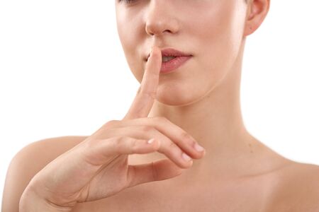 Keep my secret. Beautiful sensual woman keeping finger on lips while standing against white...