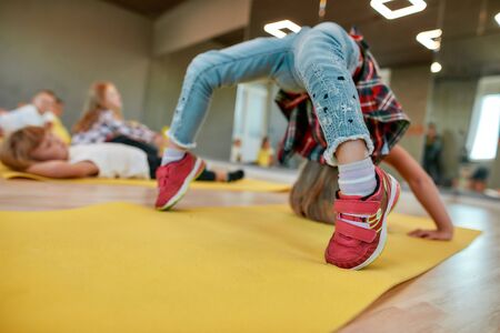 Staying flexible. Little girl making backbend on yoga mat in the dance studio. Group of children...