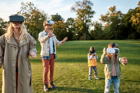 Innovative way. Family of four playing in virtual reality glasses outdoors