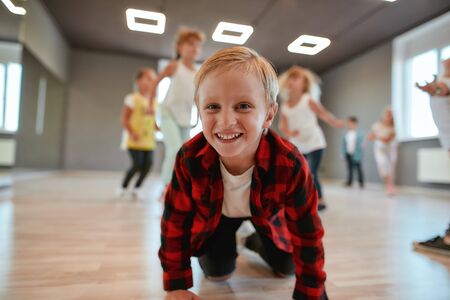 Active hobby. Portrait of funny and cute little boy in checkered flannel shirt looking at camera and smiling while having a choreography class in the dance studioの写真素材
