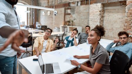 We are not just a team. Group of multicultural team listening carefully to their team leader while having business meeting in the modern officeの写真素材