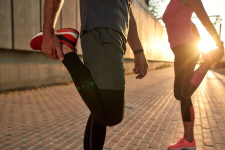 Warming up. Cropped photo of fitness couple in sports clothing doing stretching exercises before...