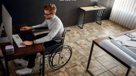 Young and creative male office worker in a wheelchair using stylus pen and digital tablet while...