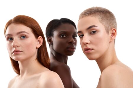 Portrait of three beautiful multicultural young women with naked shoulders posing in studio over...