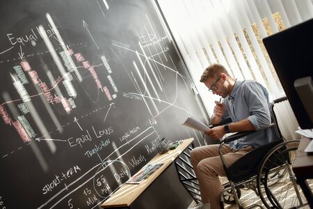 Thoughtful businessman. Concentrated young male trader in a wheelchair analyzing some documents...