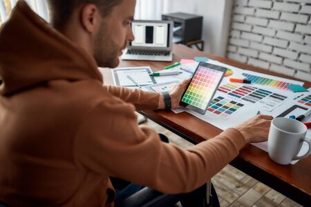 Cropped photo of focused young male UX UI designer in a wheelchair choosing color samples for new mobile app while working at his creative workplace in officeの写真素材