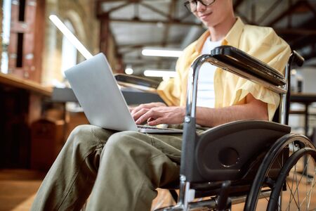 Cropped portrait of young male office worker in a wheelchair typing using his laptop while...