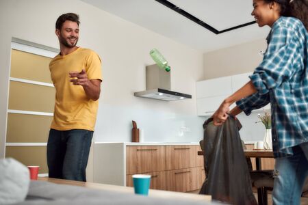 Cleaning with fun. Keeping their house clean. Young multicultural couple in casual clothes sorting garbage and smiling while cleaning their modern kitchen togetherの写真素材
