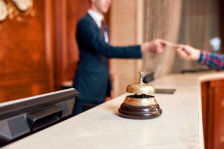 Always hear you. Young executive at the reception desk of a hotel working in the background. Focus on a service bellの写真素材