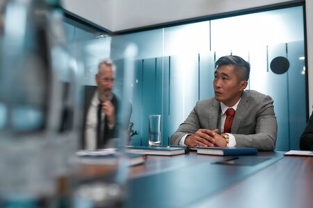 Focusing at work. Portrait of serious asian businessman in formal wear sitting at the office table in the modern officeの写真素材