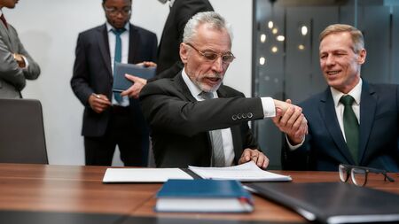 Deal. Two happy mature businessmen in classic wear shaking hands after contract signature while having a meeting in the modern officeの写真素材