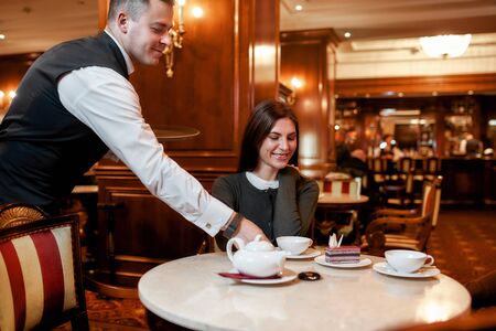 Put customers first. Confident waiter serving desserts and coffee to costumers. Couple having breakfast in hotel restaurantの写真素材