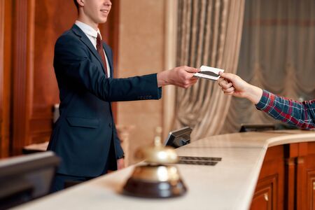 Special offers. Cropped shot of young executive at the reception desk of a hotel working, giving privileged personal card to a guestの写真素材