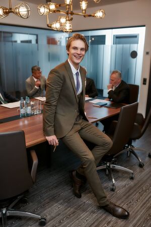 Confident and smart. Happy young businessman in formal wear looking at camera and smiling while leaning at the desk in officeの写真素材