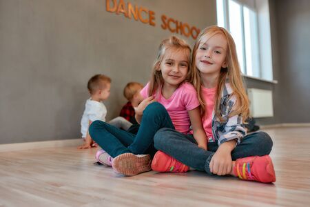 Best friends. Portrait of two happy and cute little girls in casual clothes hugging and smiling at camera while sitting on the floor in the dance studio. Active lifestyle. Choreography conceptの写真素材