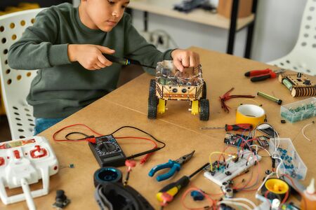 Invent. Close up of a boy using screwdriver while fixing bolts on a robot vehicle. Smart kids and STEM education.の写真素材
