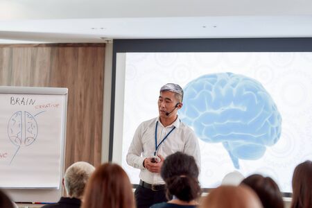 Balanced for Education. Asian male speaker in suit with headset and laser pointer giving a talk at corporate business meetingの写真素材