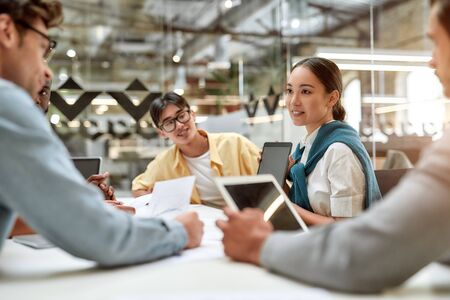 Work is easier with technologies. Young asian woman showing tablet to her colleagues and discussing something while working together in the modern officeの写真素材