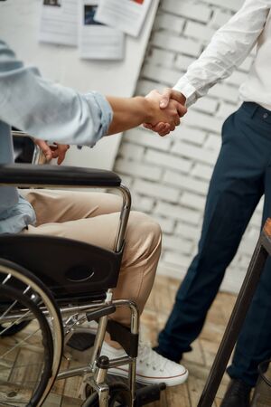 Cropped view of male office worker in a wheelchair shaking hand to his colleague while working together in the creative office. Disability conceptの写真素材