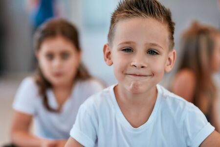 Portrait of a cute little boy in white t-shirt looking at camera and smiling while sitting on the floor in the dance studioの写真素材