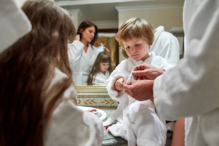Better teeth, Better health. Cropped shot of parents and two kids in white bathrobes having morning routine in hotel bathroom, near the mirror. Boy is ready to brush teeth. Family vacation conceptの写真素材