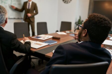 Cropped photo of young businessman in classic wear pointing at white blackboard and explaining something to his colleagues. Project team. Presentationの写真素材