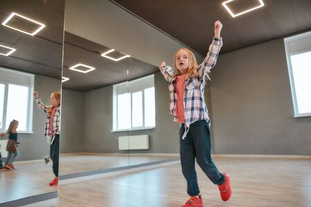 Warming up. Little cute girl raising hands up while having choreography class in studio. Dance...