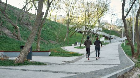 Jogging outdoors. Back view of a couple in black sportswear running together in the park. Morning...